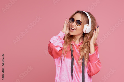 Wireless connection. Portrait of young woman in sunglasses posing isolated over pink background listening fun music with headphones. Space for text