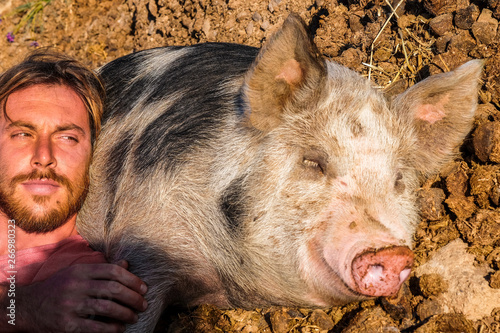 Funny portrait with attractive man with best friend big pig sleeping on the ground in nature rural country side outdoor
