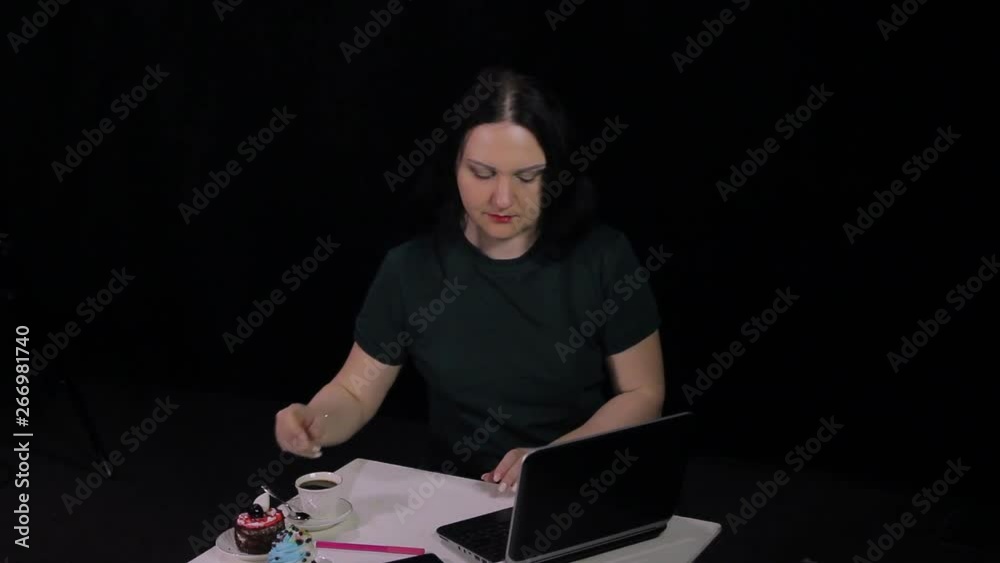 A woman at a table in a cafe typing on a keyboard with a computer and drinking coffee A woman at a table in a cafe typing on a keyboard with a computer and drinking coffee
