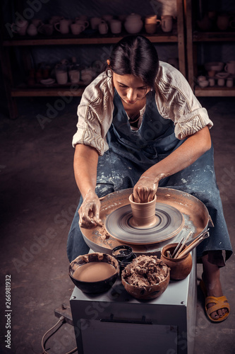 Beautiful young lady making pottery, sculptor from wet clay on wheel. Handicraft production.