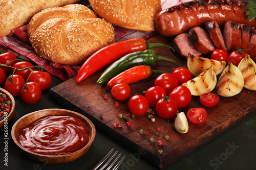 Grilled sausages with vegetables, spices and bread on wooden cutting board background