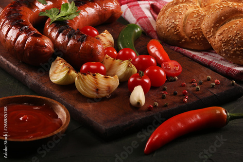 Grilled sausages with vegetables, spices and bread on wooden cutting board background