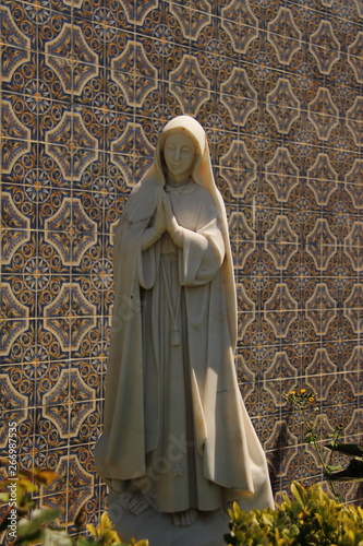 statue of Sant Maria in a garden outside home, portugal azulejos on background 