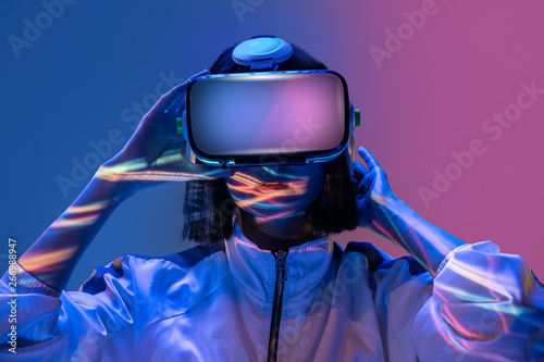 Excited young woman having virtual reality experience in neon light photo