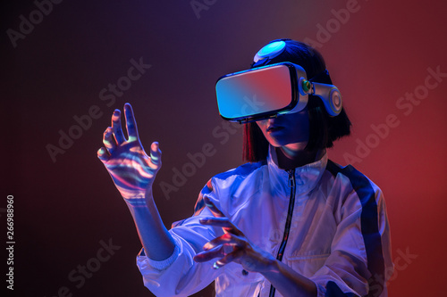 Excited young woman touching air while having virtual reality experience in neon light photo