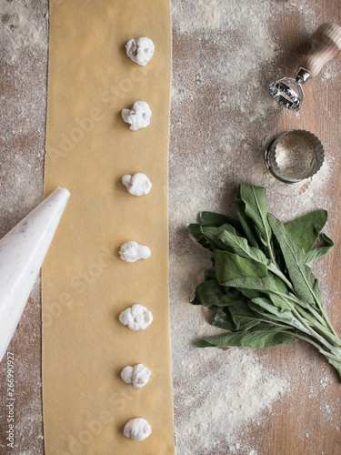 Hands of anonymous cook squeezing creamy filling on thin ravioli dough near bunch of fresh sorrel on table in kitchen photo