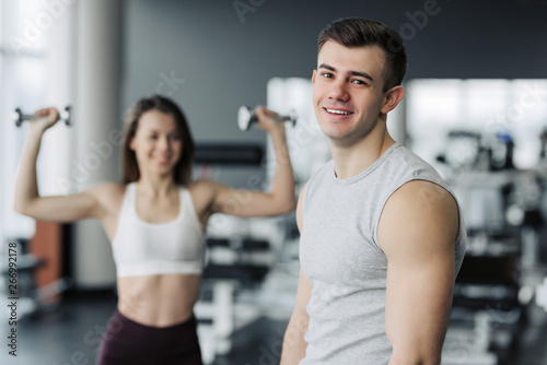 gym after strength exercises for different muscles, work out his body, push-up, squats and abs crunches with the training girl on background. Fitness, healthy and self-control concept.