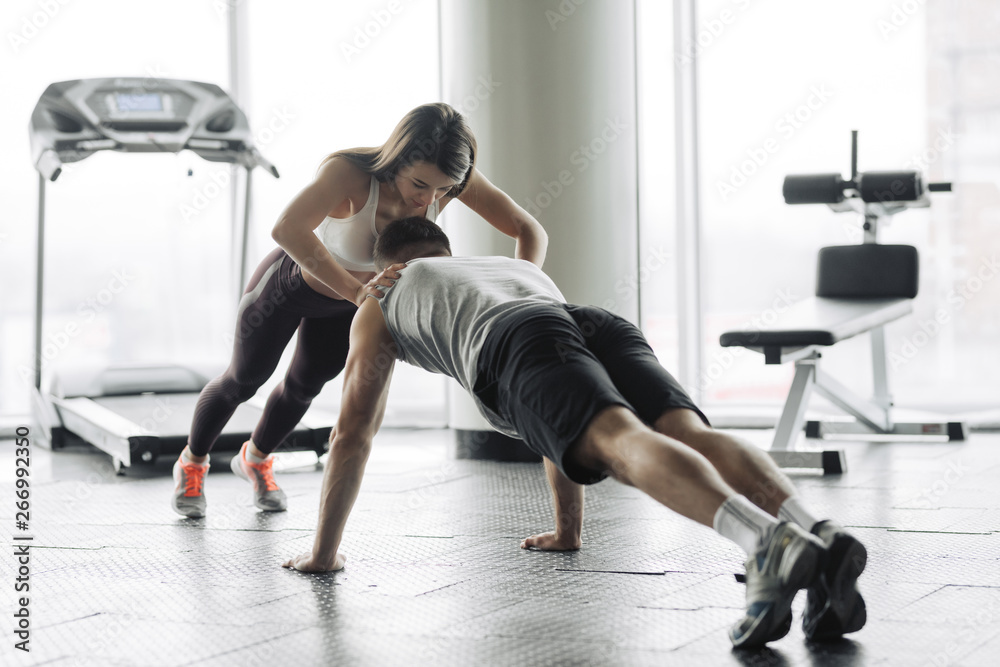 Young couple is working out at gym. Attractive woman and handsome muscular man are training in light modern gym. Double plank. Man is doing plank with girl atop.