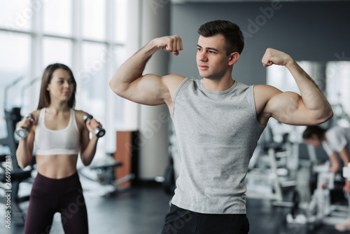 Beautiful sports couple is showing their muscles while standing in gym