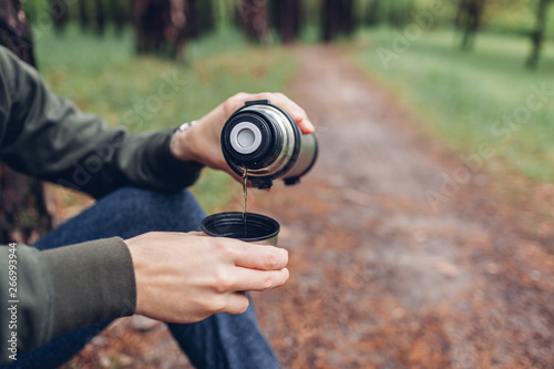 Man tourist pours hot tea out of thermos in spring forest. Camping  traveling and sport concept