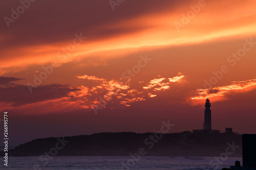 Lighthouse with colorful sunset with sun on skyline