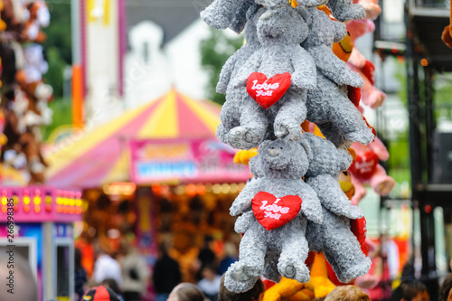 Cuddly toys with hearts saying "I Love You" hanging from a stall at a fairground