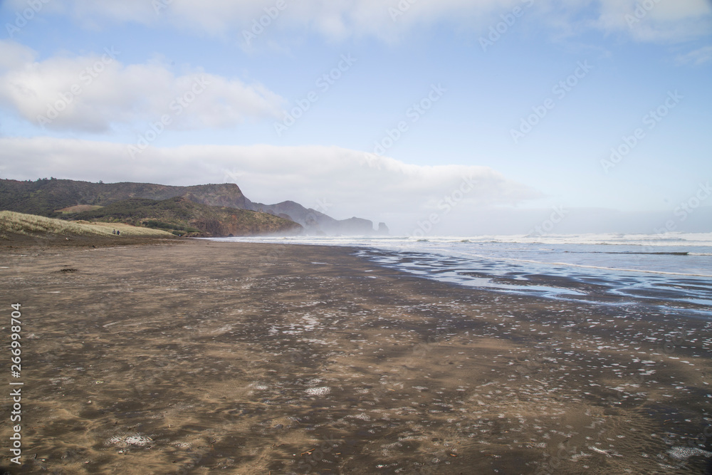 Bethells beach or Te Henga in Waitakere, West Auckland on a winters day with blue sky and white clouds. Low tide and relatively calm sea. Known for black sand, dunes and filming dramatic movies. Bethells beach or Te Henga in Waitakere, West Auckland on a winters day with blue sky and white clouds. Low tide and relatively calm sea. Known for black sand, dunes and filming dramatic movies.