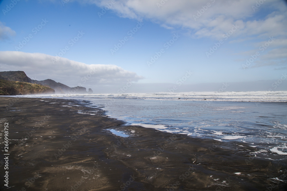 Bethells beach or Te Henga in Waitakere, West Auckland on a winters day with blue sky and white clouds. Low tide and relatively calm sea. Known for black sand, dunes and filming dramatic movies. Bethells beach or Te Henga in Waitakere, West Auckland on a winters day with blue sky and white clouds. Low tide and relatively calm sea. Known for black sand, dunes and filming dramatic movies.