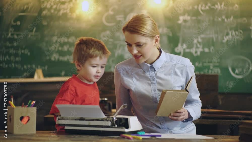 Mother and son are sitting at the table and are printing on an old typewriter in the classroom. Mother and son on the background of a green chalkboard. Little boy on extra classes with a teacher. Mother and son are sitting at the table and are printing on an old typewriter in the classroom. Mother and son on the background of a green chalkboard. Little boy on extra classes with a teacher.