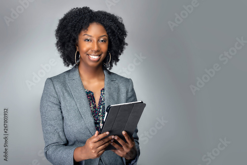 Black African American teacher or businesswoman sitting and holding a tablet computer.  The confident female author or writer looks like she is preparing for a seminar or as a keynote speaker.