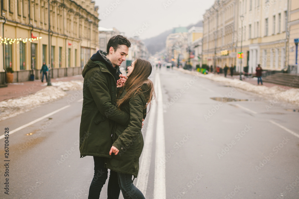 Theme love and romance. Caucasian young people heterosexual couple in love students boyfriend girl hugging and kissing on center of road in center of European city. Man woman happiness love and youth
