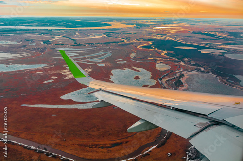 Colorful top view of the spring northern tundra and lakes from the airplane porthole. Also visible is the wing of the flying plane.