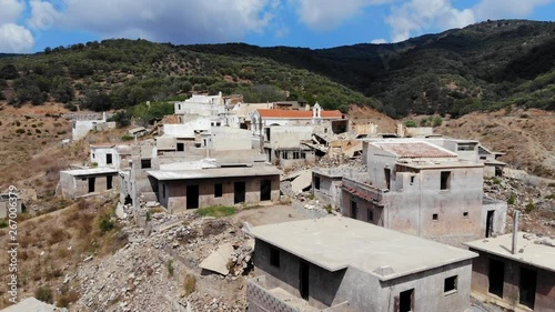 Abandoned houses and broken buildings, aerial shot, camera fly back, reveal panorama of Sfendili village at hill slope. Green mounts on background, dry land around forsaken place photo