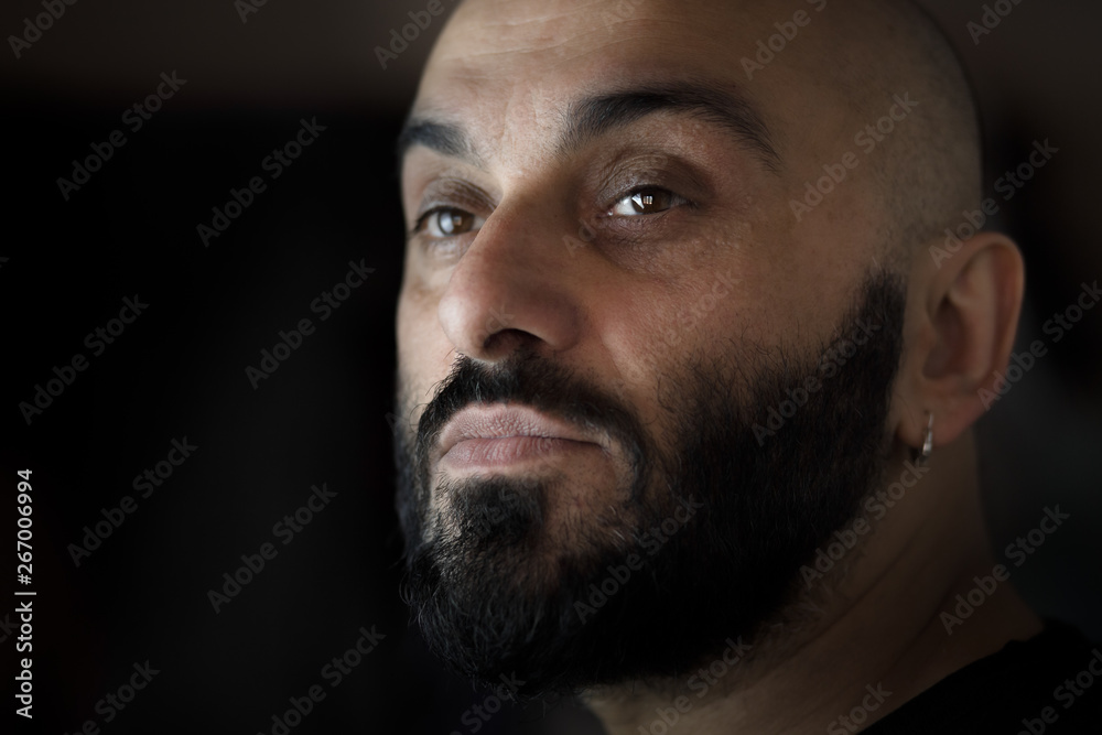 Fototapeta premium Close-up portrait of a bearded bald man with earring with black, dark background