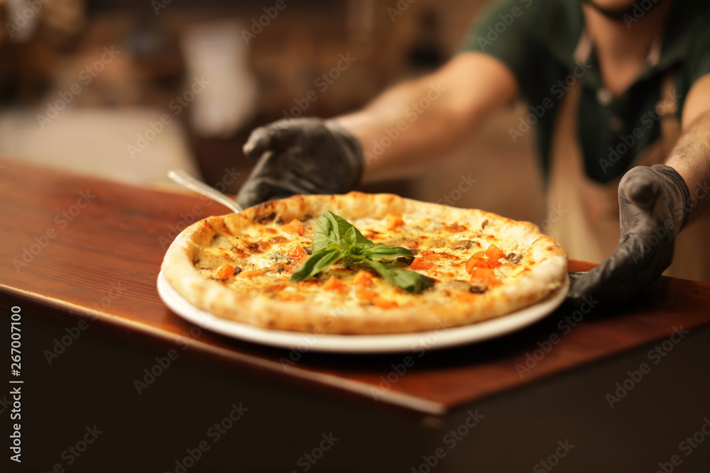 Man holding plate with oven baked pizza on table, closeup