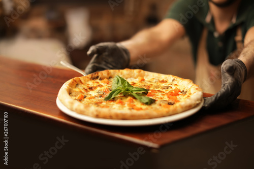 Man holding plate with oven baked pizza on table  closeup