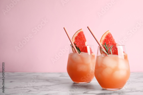 Glasses of grapefruit cocktails on table against color background. Space for text photo