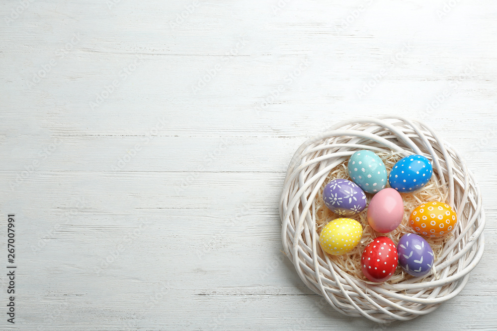 Wicker nest with painted Easter eggs on wooden table, top view. Space for text Wicker nest with painted Easter eggs on wooden table, top view. Space for text