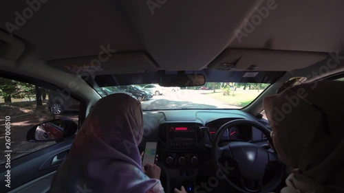 Two young Asian Muslim women in car, driving a car as pilot and as co pilot, pov from back seat inside the car. Co pilot using navigation map on the smartphone. photo