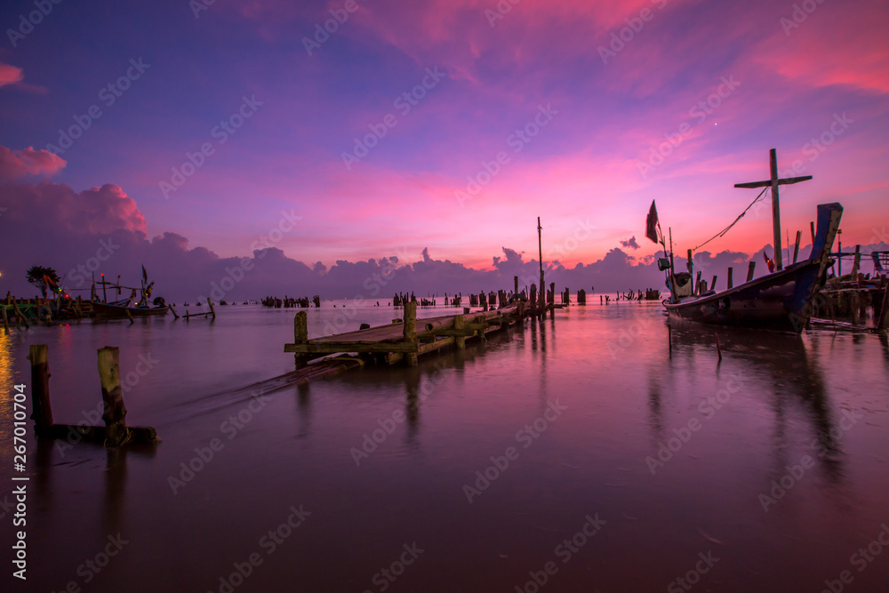 The blurred background of the morning twilight by the sea, changing the color of the beautiful sky, there is a fishing boat docked waiting to go out to find fish again.