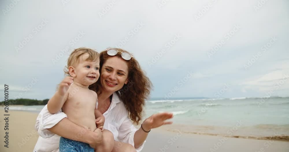Caucasian mother playing with her adorable baby on the seashore, showing gestures. Cute child happily smiling - parenthood concept 4k slow motion Caucasian mother playing with her adorable baby on the seashore, showing gestures. Cute child happily smiling - parenthood concept 4k slow motion