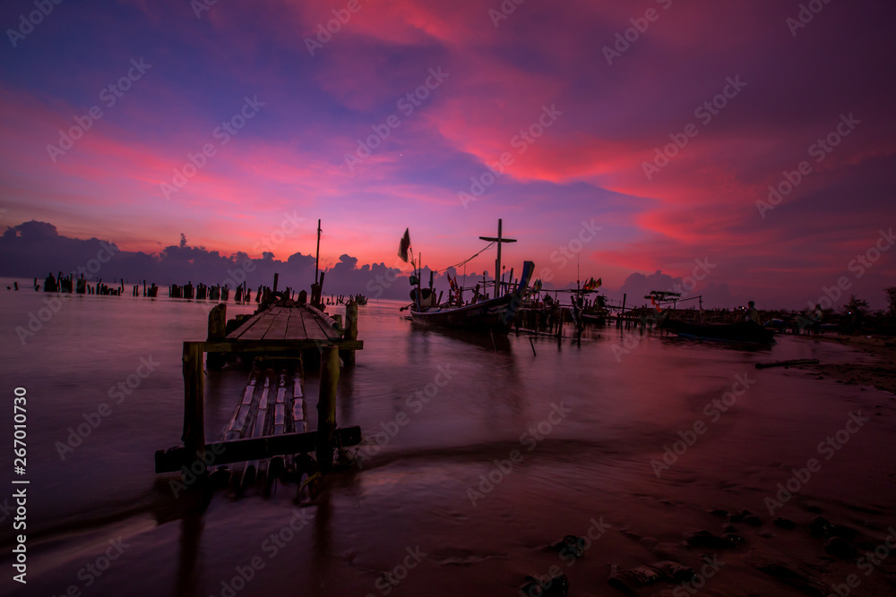 Obraz premium The blurred background of the morning twilight by the sea, changing the color of the beautiful sky, there is a fishing boat docked waiting to go out to find fish again.