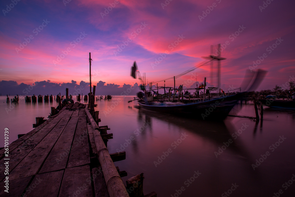 The blurred background of the morning twilight by the sea, changing the color of the beautiful sky, there is a fishing boat docked waiting to go out to find fish again.