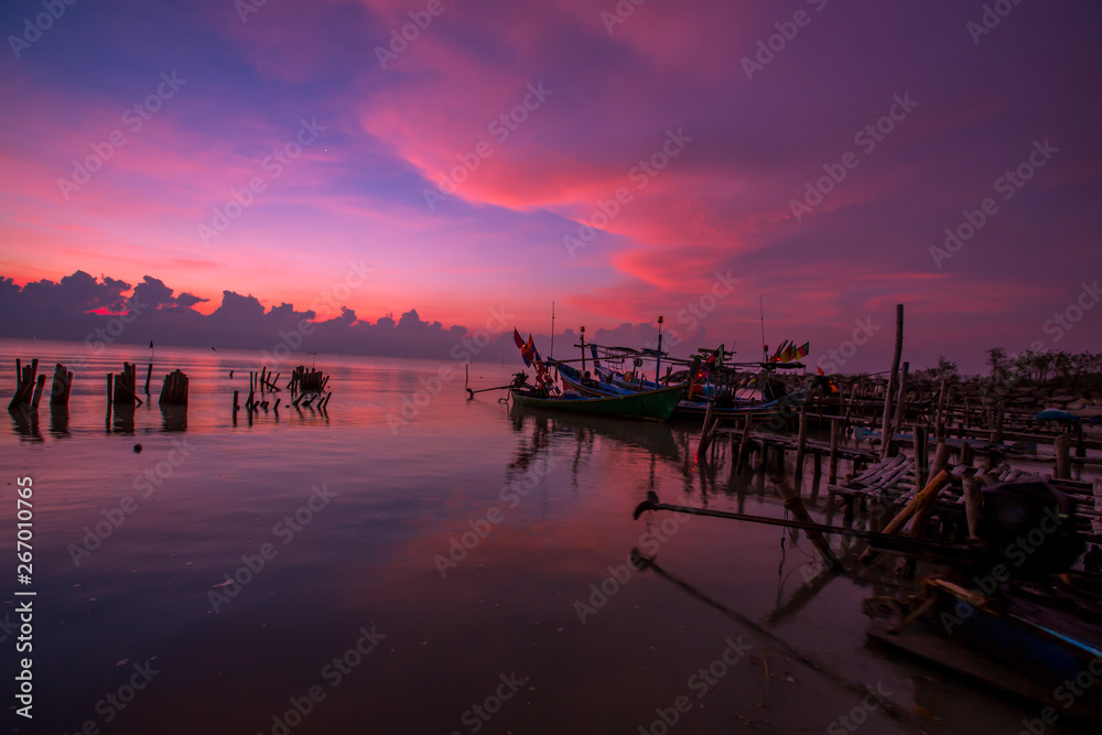 Obraz premium The blurred background of the morning twilight by the sea, changing the color of the beautiful sky, there is a fishing boat docked waiting to go out to find fish again.