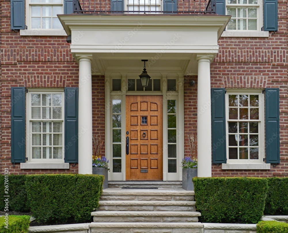 front of elegantly landscaped house with stone steps and portico over wooden front door
