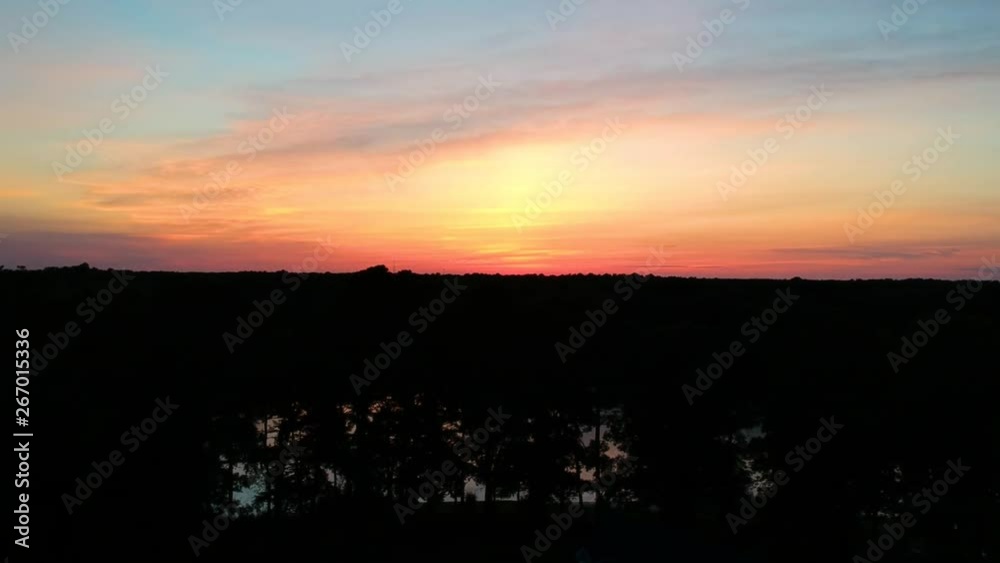 An aerial drone shot of the silhouetted forest and bay against a colorful sunset. An aerial drone shot of the silhouetted forest and bay against a colorful sunset.