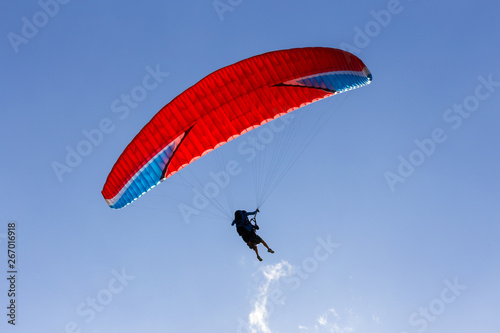 A silhouette of a paraglider with red chute floating across the blue sky