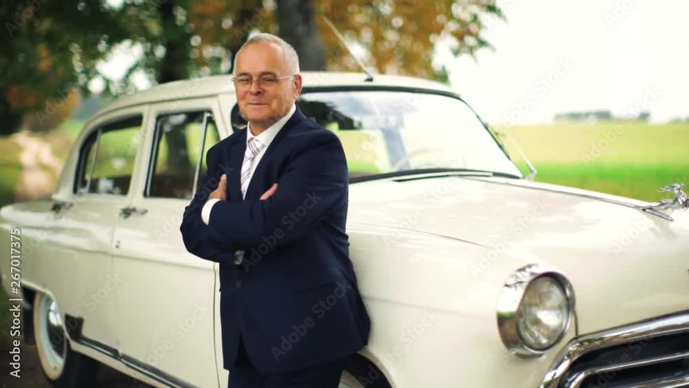 An elderly man standing near an expensive car. An old businessman in a suit. An elderly rich man standing near the car. Happy old age. An elderly man standing near an expensive car. An old businessman in a suit. An elderly rich man standing near the car. Happy old age.