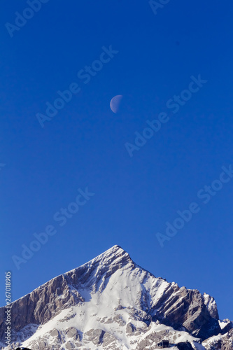 moon on the blue sky over snow covered mountain peaks
