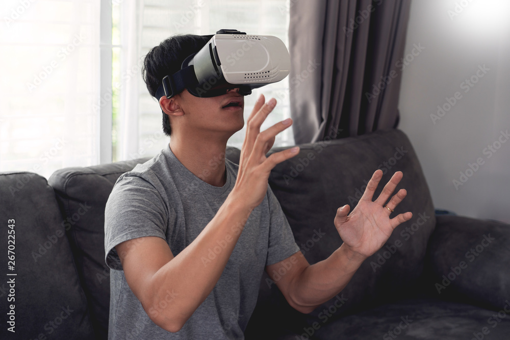 Obraz premium a cheerful man sitting on couch and wearing 3D virtual reality glasses.