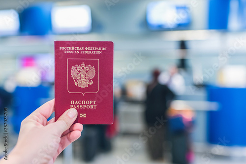 Female holding russian pasport opposite airport board.