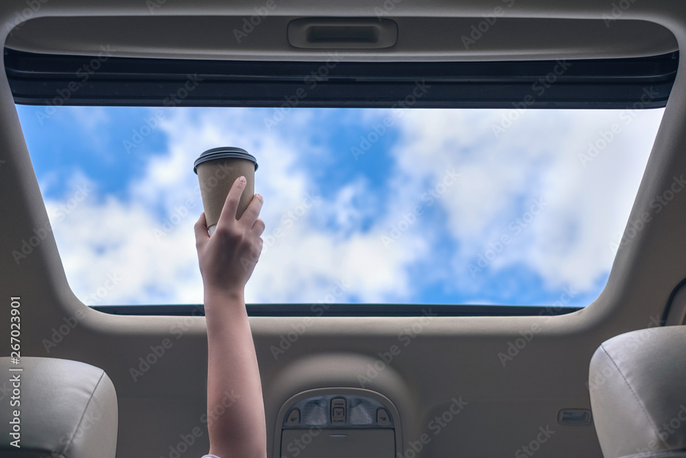 Naklejka premium Girl passenger holding paper cup of coffee in open hatch of a car. Travel concept