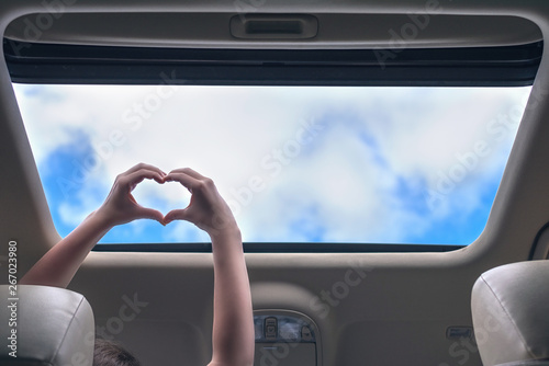 Картината върху платно girl traveling by car and holds her hands in the form of heart out from open hatch of a vehicle