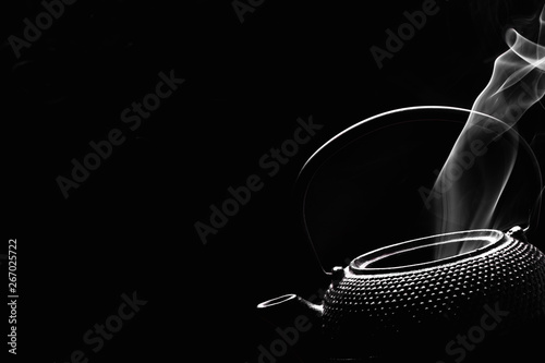 Rustic tea pot on black background. Steaming teapot. Cooking concept.