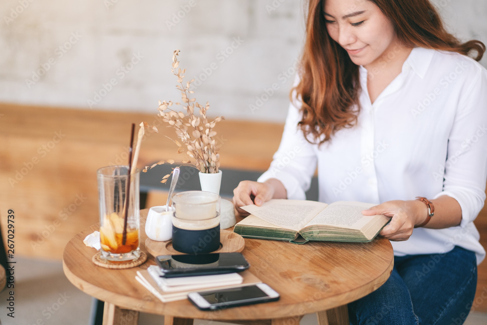 Closeup image of a beautiful asian woman holding and reading a book while sitting in cafe Closeup image of a beautiful asian woman holding and reading a book while sitting in cafe