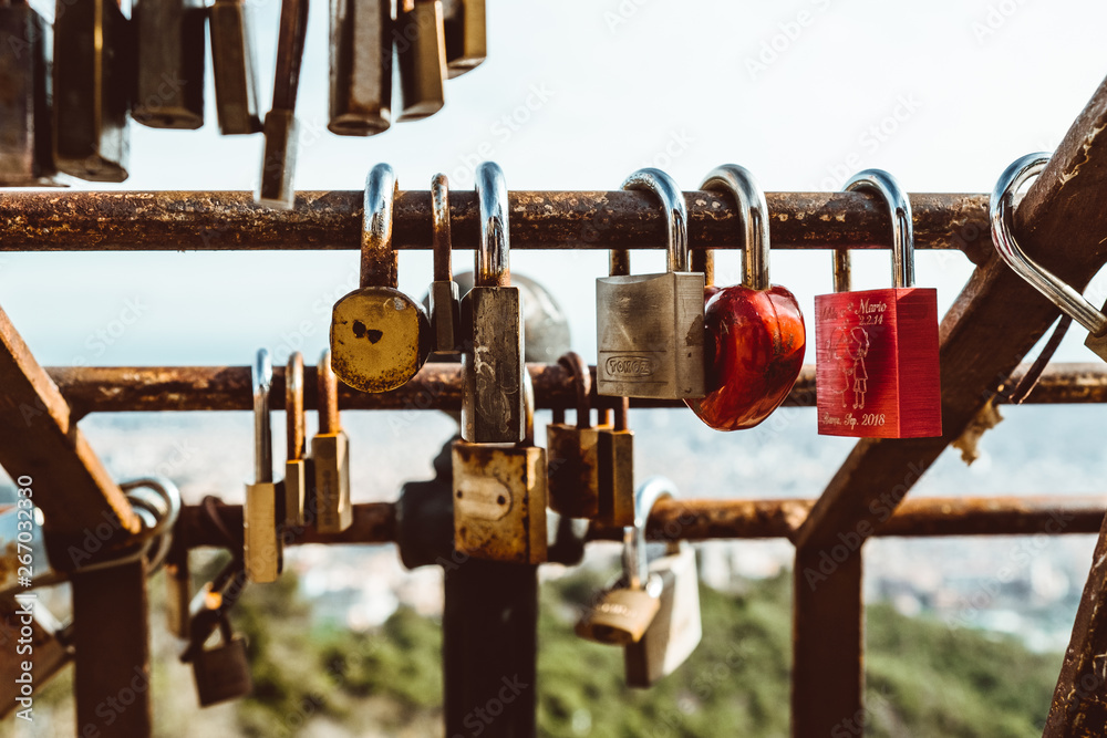 padlocks on rusty bar with blurred view of Barcelona from Tibidabo mountain on sunny summer day