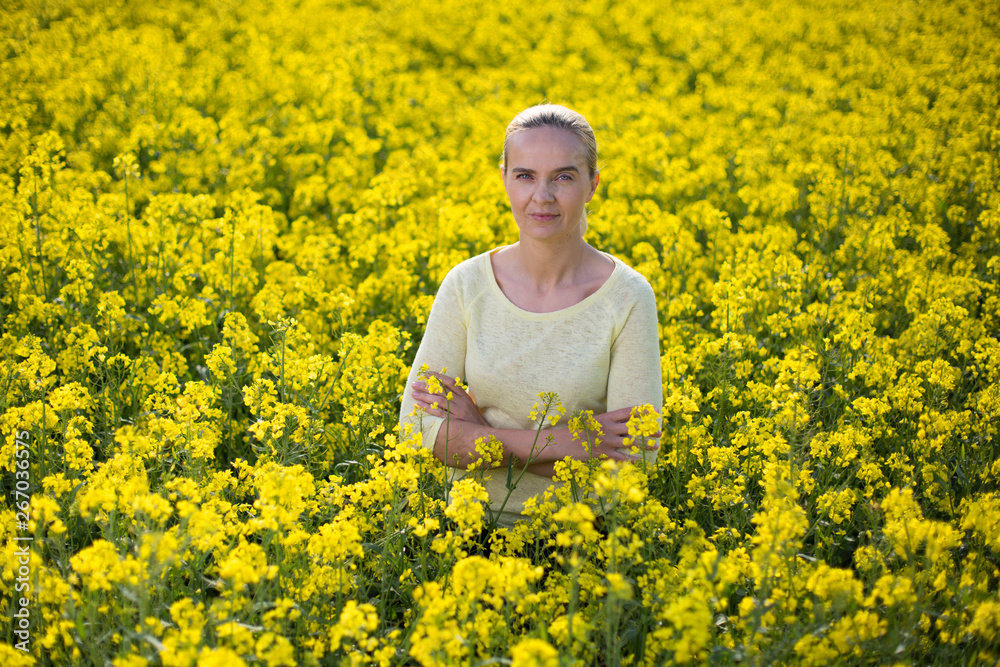 Fototapeta premium Happy woman on blooming rapeseed field in springin yellow blouse.