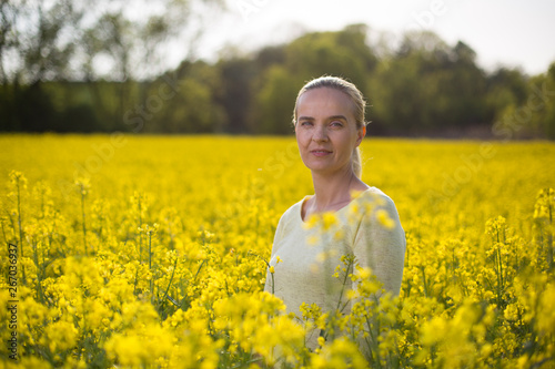Happy woman on blooming rapeseed field in springin yellow blouse.