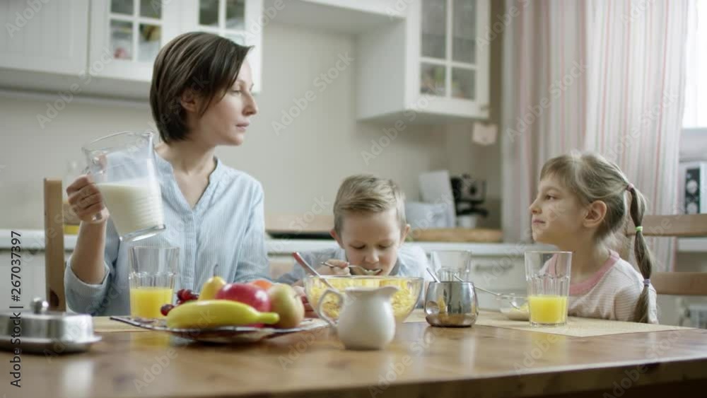 mother communicate during breakfast with her children and add additional milk to children's cornflakes bowls mother communicate during breakfast with her children and add additional milk to children's cornflakes bowls