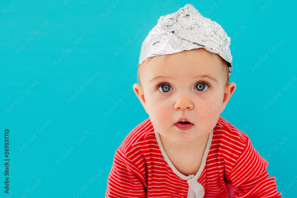 A child in a foil hat sits on a blue background A child in a foil hat sits on a blue background